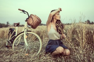 Ung kvinde i udkanten af en mark med sin cykel og cykelkurv